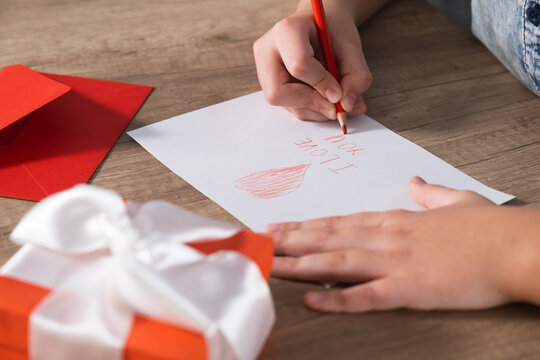 Child hands draws a greeting card and writes I love you in red pencil. Congratulations for Mother's Day or Valentine's Day holiday.