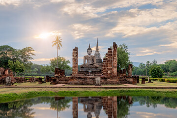 Buddha statue and pagoda Wat Mahathat temple with reflection during sun set, Sukhothai Historical Park, Thailand