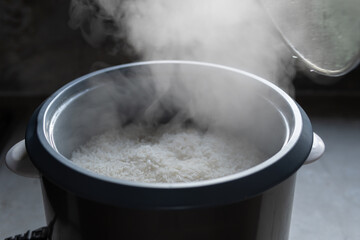 The steam from A man hand lifting a glass lid off electric rice cooker in the kitchen.hot food concept