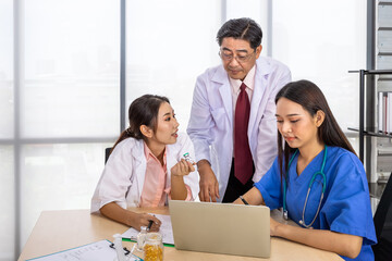 Fototapeta premium Asian male and female medical doctor team sitting at desk and meeting discussion about vaccine with laptop computer
