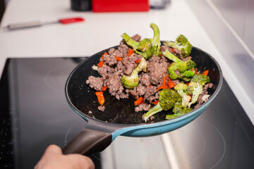 Skillet of ground beef stir fry with vegetables broccoli pepper and onion on an electric stove on high speed Cordoba Argentina