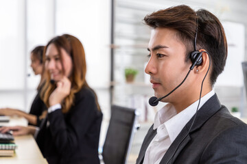 Young Asian male customer service support agent operator team working in call center office with headsets and computer.