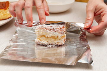 BOLO GELADO is a traditional Brazilian cake -  Wrapping the cake with coconut sprinkles in aluminum foil. Front view.