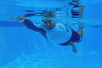 Man swimming in blue water. Sportsman training in blue swimming pool. Swimming pool underwater photography. Young man in swimwear. Fitness and active lifestyle training