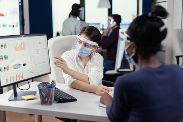 Coworkers wearing face mask checking corporate statistics during coronavirus. Multiethnic team working in company with new normal respecting social distance.