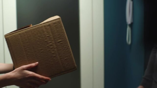 Close-up of woman receiving parcel at home from delivery man hands on doorstep at apartment. Courier male delivering package, closeup, side view. Concept of online shopping. Shooting in slow motion.
