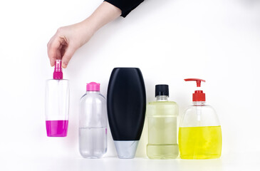 Isolated bottles of detergents on a white background. The hand takes the jars of detergents. In the photo, shampoo, micellar water, liquid soap and mouthwash. Household chemicals in colored containers