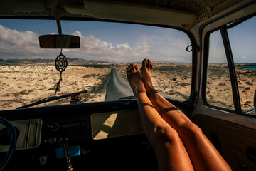 Travel and freedom concept people with close up of woman legs enjoy the road trip inside an old vintage van - vanlife lifestyle girl with long road asphalt in background - obrazy, fototapety, plakaty