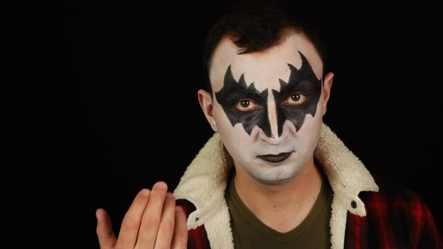 Man in demon makeup making inviting gesture to camera on black background