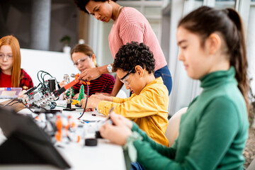 African American female science teacher with group of kids programming electric toys and robots at robotics classroom