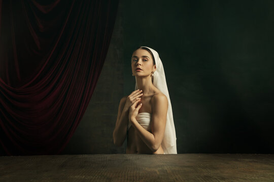 Tender. Modern remake of classical artwork - young medieval woman in white cloth on dark studio background posing beautiful and inspired. Concept of beauty, comparison of eras, creativity, art.