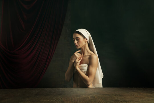 Sadness. Modern remake of classical artwork - young medieval woman in white cloth on dark studio background posing beautiful and inspired. Concept of beauty, comparison of eras, creativity, art.