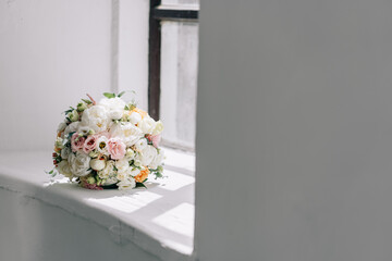 wedding bouquet with hydrangeas and roses lies on a white windowsill near the window with louis sun