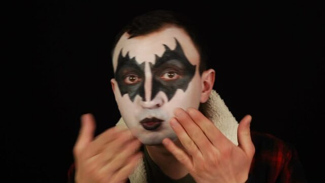 Man in demon makeup sending air kisses on black background