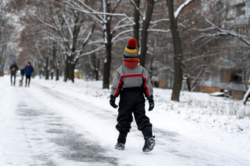 Fototapeta na wymiar Boy walks in the winter park. Child walks along snowy road. Back view
