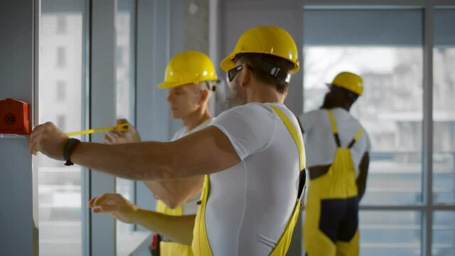Male industrial builder workers measuring windows with ruler