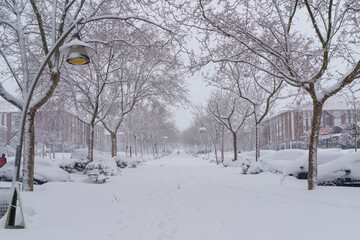 Fototapeta premium Streets and buildings covered in snow by day due to snowstorm Filomena falling in Madrid Spain. People walking in the snow. 