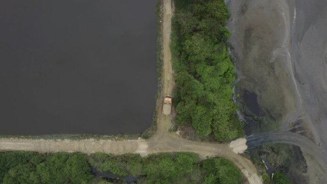 A large truck riding over a small dirt road next to the water to bring it's sand load to the destined area 
