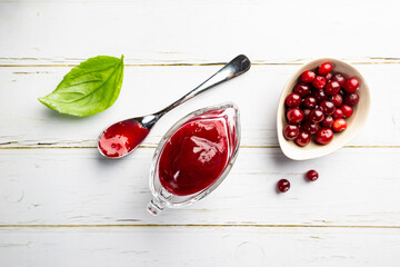 Homemade cranberry sauce for meat and fish in glass gravy boat on white background. top view