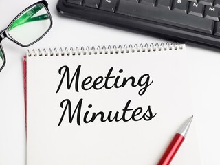 Top view text Meeting Minutes written on note book with pen,eye glasses and keyboard.Business concept.