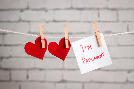 Valentine's day composition. Red hearts hanging on the clothespins. with a note "I'm pregnant". Conceptual image for February 14th. 