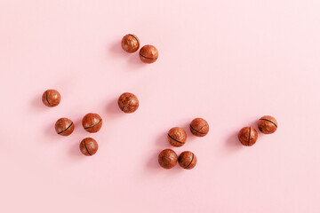 Raw macadamia nut scattered on a pink solid background. Minimal composition.