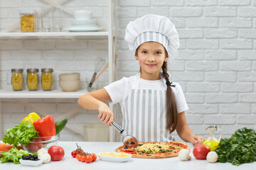 cute little girl in chef hat and an apron cutting pizza at kitchen