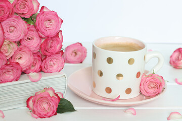 Cup of coffee, pink roses and closed book on the table. Mothers Day, Birthday, Valentines Day, Womens Day, celebration concept. Selective focus.