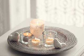 Beautiful burning candles on tray against light background