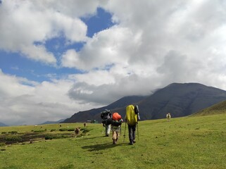 Fototapeta premium Back view of group of alpinist, hikers with backpacks going to the mountains in cloudy, warm weather