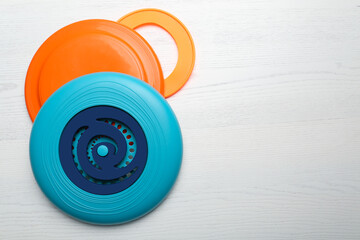Plastic frisbee disks and ring on white wooden background, flat lay. Space for text