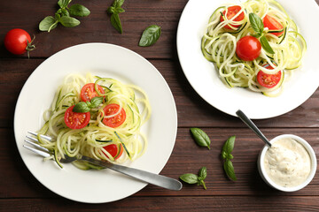 Tasty zucchini pasta with tomatoes and basil served on wooden table, flat lay