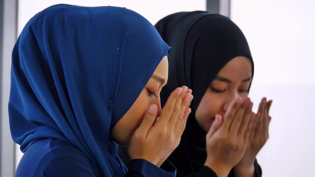 Two Asian Muslim young women in traditional hijab are praying glorify Allah and practicing the Islamic faith in mosque.