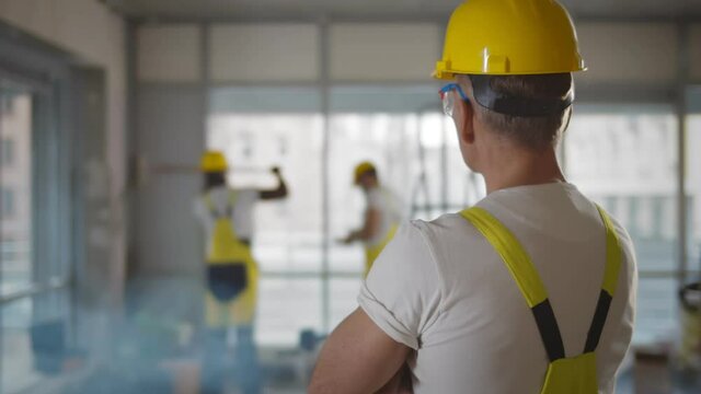 Back view of foreman in yellow hardhat watching crew doing renovation