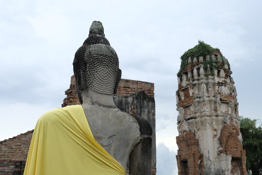 Back of old ruins buddha yellow cloth cover on buddha shoulder ,Thai histry and architecture in Wat Mahathat in Buddhist temple,Siam capital Ayutthaya religious of Thailand.