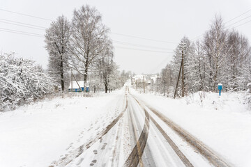 Rural road with a mountain and traces of car tires, poles with power lines and dirty asphalt with salt
