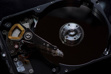 Component parts of a disassembled hard drive, close-up on a dark background.