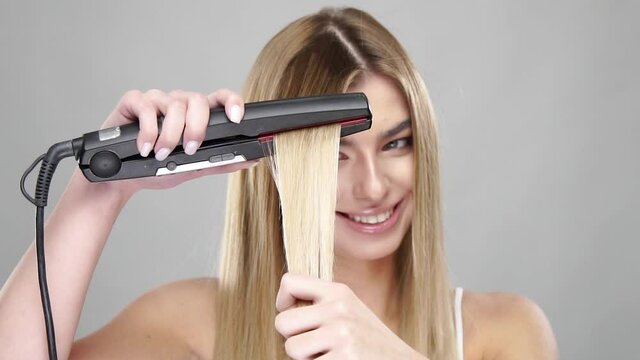 blonde woman straightens hair on grey background