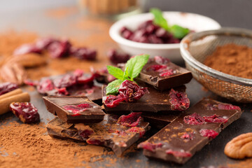Homemade dark chocolate bar with dried berries, nuts and cinnamon on black background.