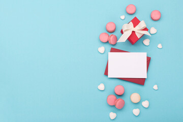 White glitter hearts, gift box, sweets macaroons and empty card on blue background. Valentines Day, Happy Women's Day, Mother's day concept. Top view, copy space.