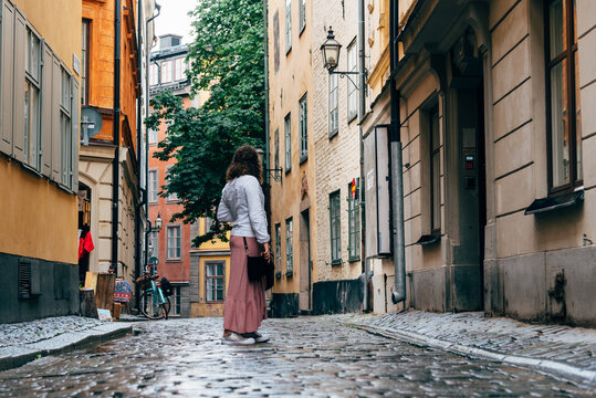 Beautiful young woman is looking back in a picturesque and narrow cobblestoned street amidst old buildings in Gamla Stan quarter in Stockholm