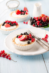Homemade Tartlets with cream and fresh berries on blue wooden table.