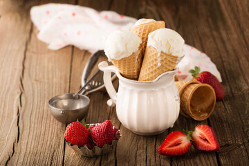 Homemade Vanilla ice cream in waffle cones with fresh strawberries on wooden background.