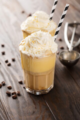 Iced coffee with whipped cream and caramel ice cream in tall glasses on rustic wooden background.