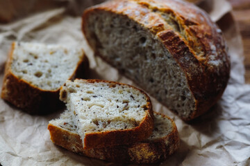 Homemade bread with cereals lies on rough craft paper. Delicious and fresh pastry made with your own hands. Photo with light from the window.