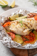 Foil with baked fish and vegetables. Baked cod fillet with zucchini, tomatoes, thyme and rosemary close-up.
