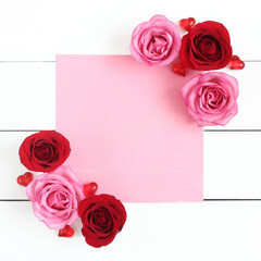 Pink and red roses with hearts. Pastel pink empty paper on white wooden background.  Space for text.