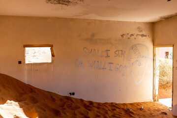 Neglected house interior buried in the sand in village Al Madam in United Arab Emirates, with spooky inscription: 'Shall I stay or shall I go' on the wall.