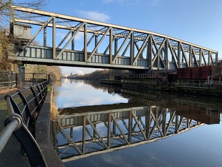 Old metal bridge going over the Manchester ship canal with reflections in the water and a blue sky background. 