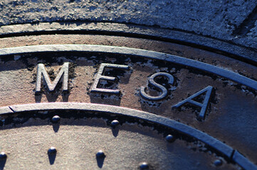 Close-up of a weathered manhole cover in Mesa, Arizona, with the word 'MESA' prominently embossed,...